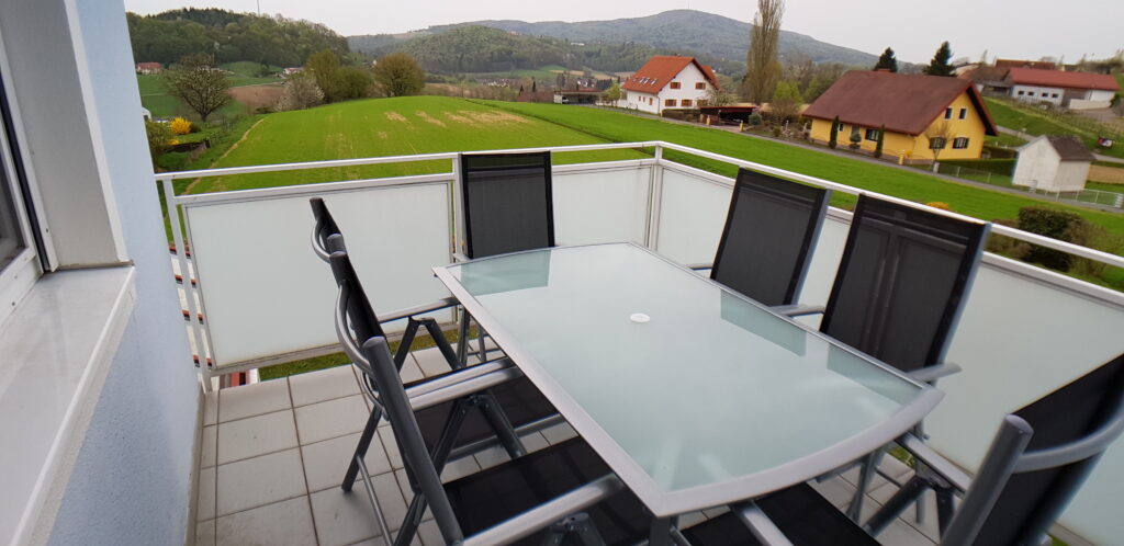 Balkon der Ferienwohnung mit Tisch, Stühlen und Blick über die Hügel des steirischen Vulkanlands